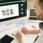 Busy software developer sitting at desktop computer and typing on keyboard while setting up computer program in modern office