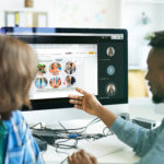 Busy young interracial colleagues analyzing computer code on computer: African man pointing at monitor and asking coworker in office